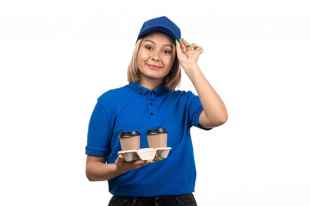 A front view young female courier in blue uniform holding coffee cups