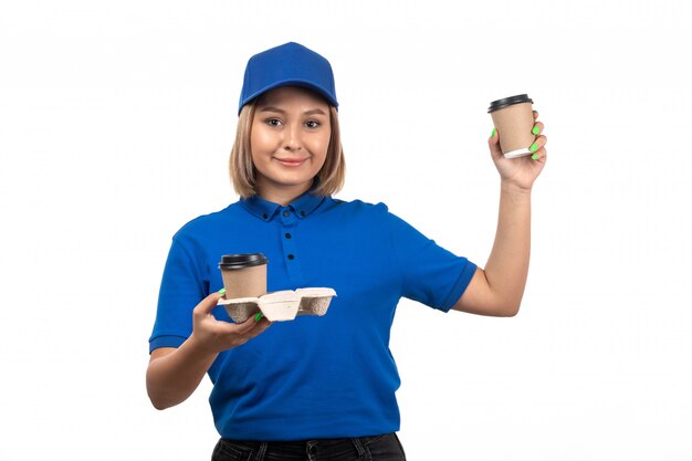 A front view young female courier in blue uniform holding coffee cups