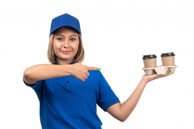 A front view young female courier in blue uniform holding coffee cups