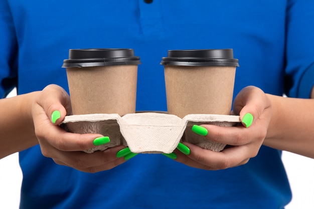 A front view young female courier in blue uniform holding coffee cups