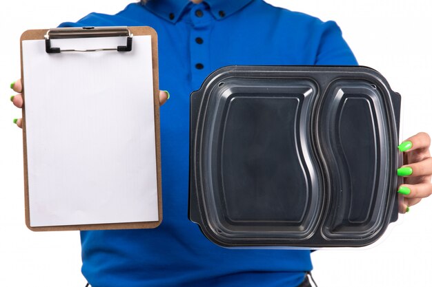 A front view young female courier in blue uniform holding food delivery bowl and notepad for signatures