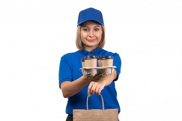 A front view young female courier in blue uniform holding food delivery package and coffee cups