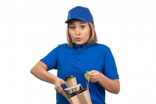 Молодая женщина-курьер в синей форме, держащая пакет для доставки еды и кофейные чашки, вид спереди
