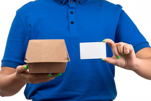 A front view young female courier in blue uniform holding food delivery package and white card