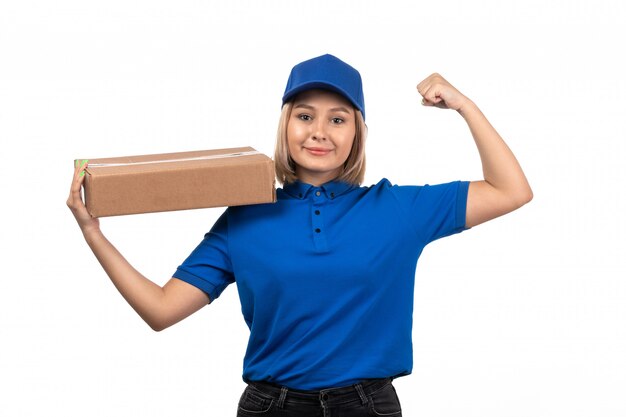 Молодая женщина-курьер в синей форме, держащая пакет для доставки еды с улыбкой на лице, вид спереди
