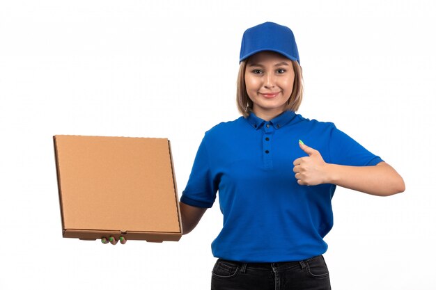 A front view young female courier in blue uniform holding food delivery package with smile on her face