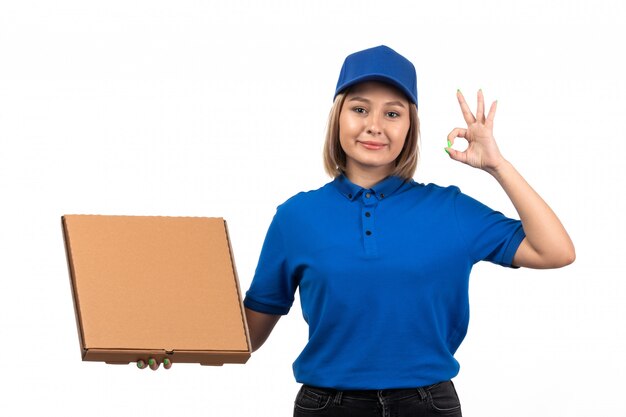 A front view young female courier in blue uniform holding food delivery package with smile on her face