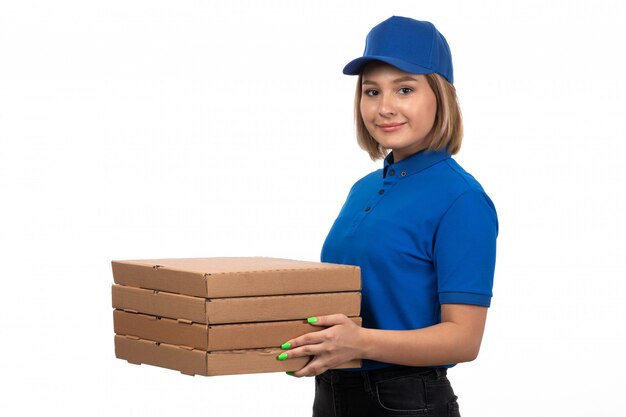 A front view young female courier in blue uniform holding food delivery packages with smile