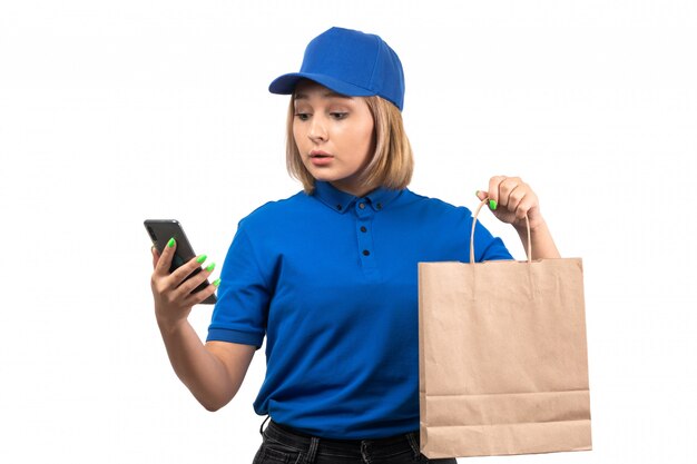 Молодая женщина-курьер в синей форме, держащая телефон и пакет для доставки еды, вид спереди