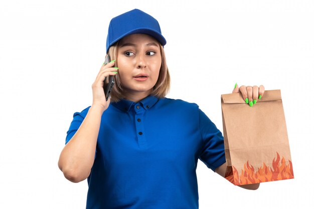 Молодая женщина-курьер в синей форме, держащая телефон и пакет для доставки еды, вид спереди