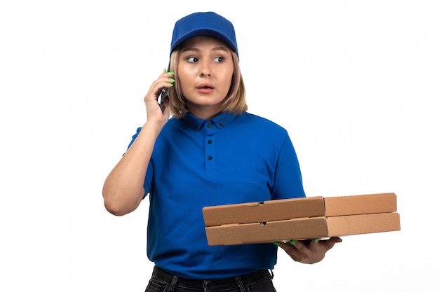 A front view young female courier in blue uniform holding phone and food delivery packages