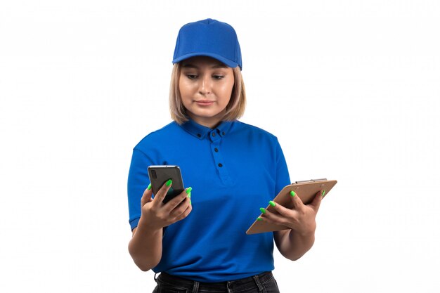 A front view young female courier in blue uniform holding phone and notepad