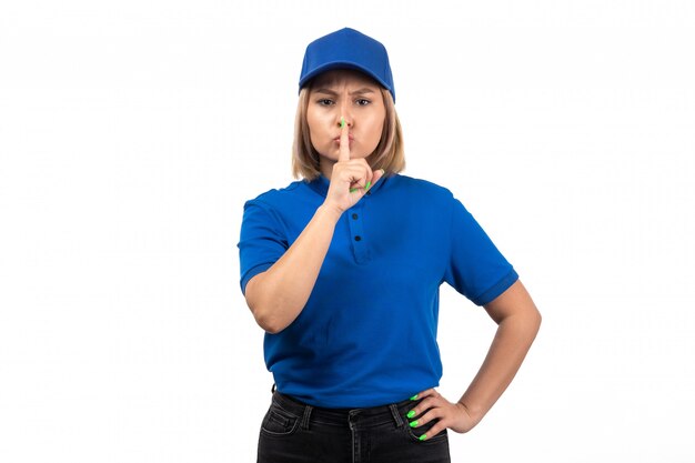 A front view young female courier in blue uniform just posing and showing silence sign