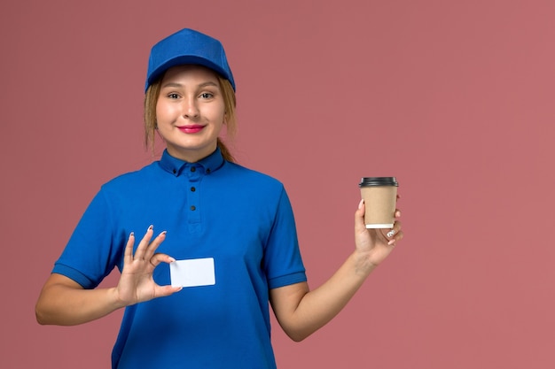 Giovane corriere femminile di vista frontale in uniforme blu che posa che tiene la tazza di caffè marrone di consegna, lavoro della donna di consegna dell'uniforme di servizio