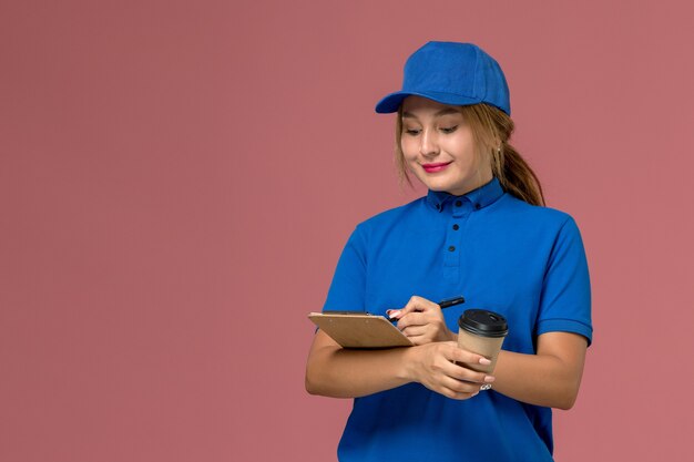 コーヒーとメモ帳のカップを保持している青い制服ポーズの正面図若い女性の宅配便、サービス制服配達女性労働者