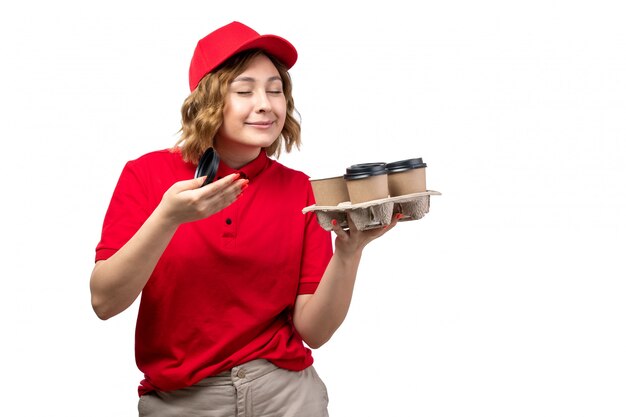 A front view young female courier female worker of food delivery service holding coffee cups smeling on white