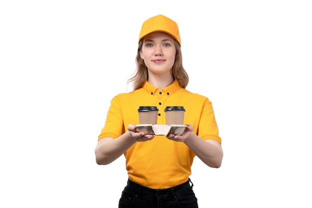 A front view young female courier female worker of food delivery service holding coffee cups and smiling on white