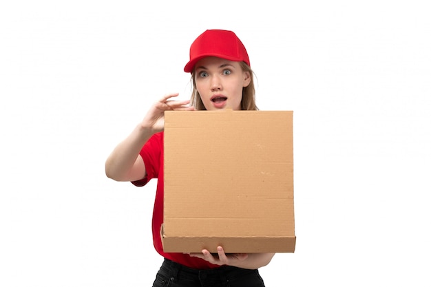 A front view young female courier female worker of food delivery service holding delivery box opening it with surprised expression on white