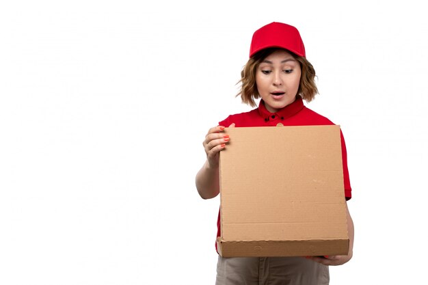 A front view young female courier female worker of food delivery service holding food delivery box opening it on white