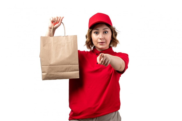 A front view young female courier female worker of food delivery service holding food delivery package pointing the camera on white
