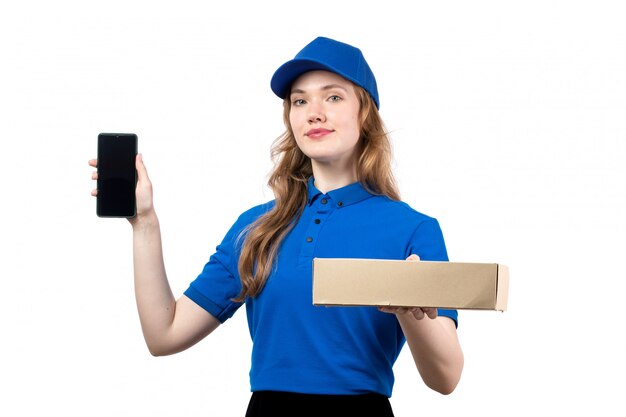 A front view young female courier female worker of food delivery service holding food delivery package and smartphone on white