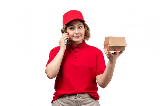 A front view young female courier female worker of food delivery service holding food package and smiling on white