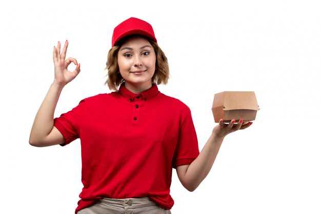 A front view young female courier female worker of food delivery service holding food package and smiling on white