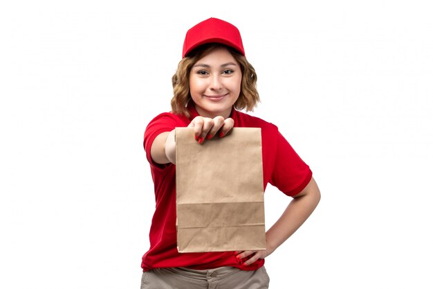 A front view young female courier female worker of food delivery service holding food package smiling on white