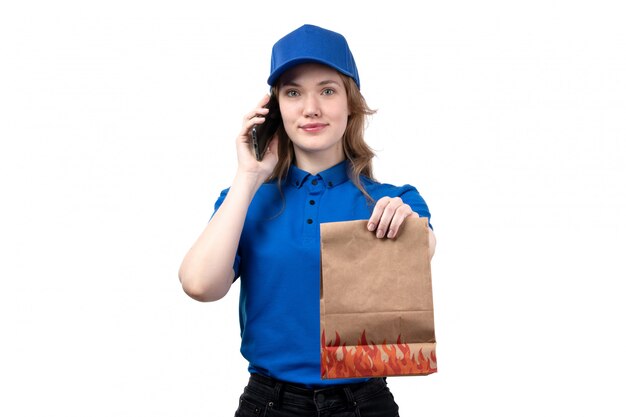 A front view young female courier female worker of food delivery service holding food package and talking on phone on white