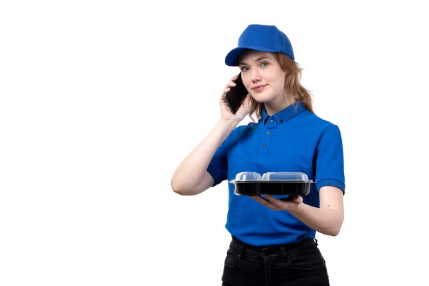Вид спереди молодой женщины курьер работница службы доставки еды, улыбаясь, держа миску с едой во время разговора по телефону на белом