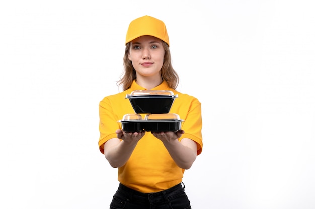 A front view young female courier female worker of food delivery service smiling holding bowls with food on white