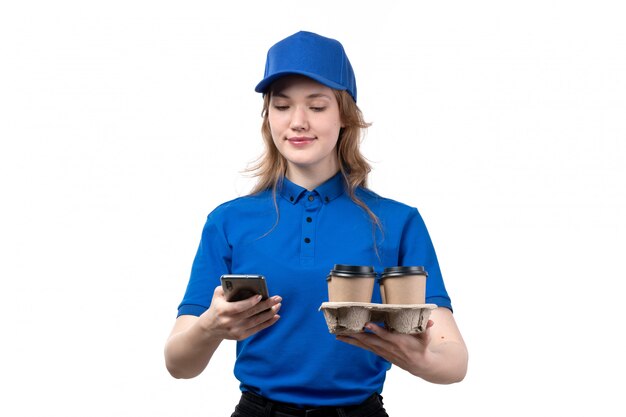 正面から見た若い女性の宅配便のフードデリバリーサービスの女性労働者がコーヒーを保持しているカップを笑顔で携帯電話を使用