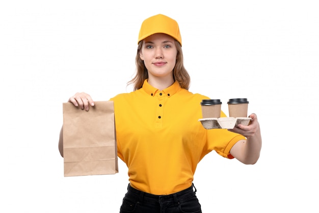 A front view young female courier female worker of food delivery service smiling holding food package and coffee cups on white