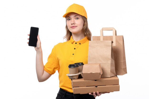 A front view young female courier female worker of food delivery service smiling holding food packages and coffee cups along with smartphone on white