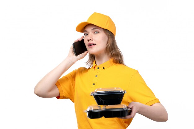 A front view young female courier female worker of food delivery service talking on phone holding bowls with food on white