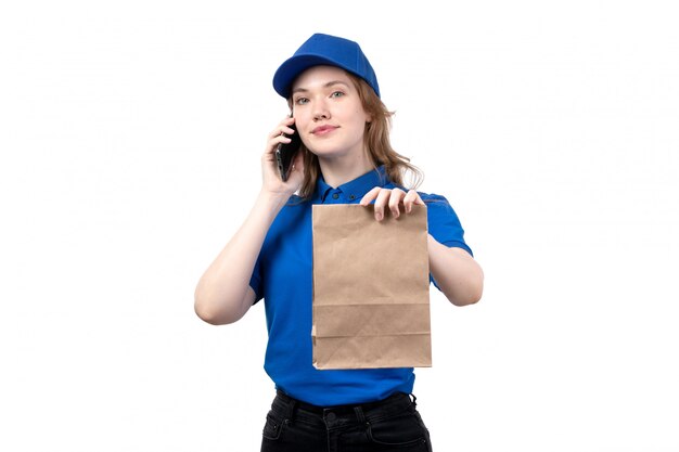 Вид спереди молодая женщина-курьер работница службы доставки еды разговаривает по телефону и держит пакет с продуктами на белом