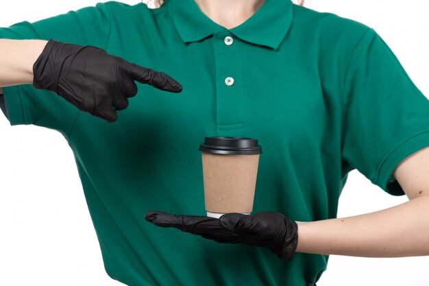 A front view young female courier in green uniform black gloves and black mask holding coffee cup