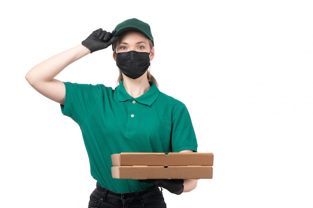 Молодая женщина-курьер в зеленой униформе, черные перчатки и черная маска, держащая коробки для доставки еды, вид спереди