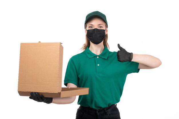 Вид спереди молодая женщина-курьер в зеленой форме, черные перчатки и черная маска, держащая доставку посылки с доставкой