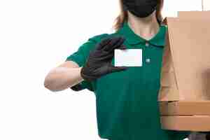 Free photo a front view young female courier in green uniform black gloves and black mask holding food delivery packages delivering