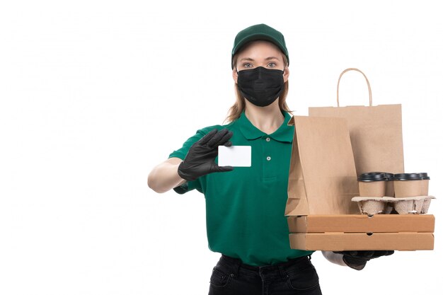 A front view young female courier in green uniform black gloves and black mask holding food delivery packages delivering