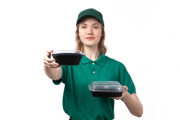 A front view young female courier in green uniform holding bowls with food on white