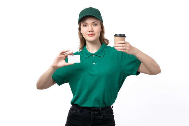 A front view young female courier in green uniform holding coffee cup and white card on white