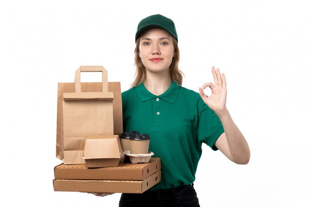 A front view young female courier in green uniform holding coffee cups and food delivery packages on white