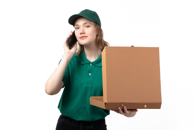 A front view young female courier in green uniform holding food delivery package and talking on the phone