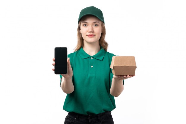 A front view young female courier in green uniform holding food package and smartphone