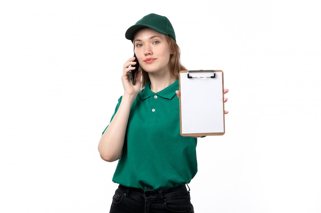 A front view young female courier in green uniform holding notepad for signatures while talking on the phone