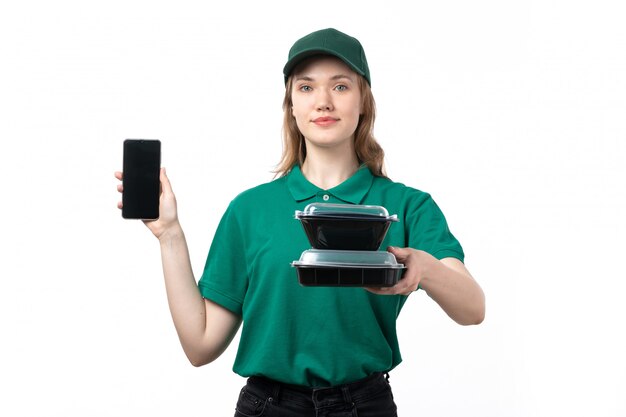 A front view young female courier in green uniform holding smartphone and bowls with food