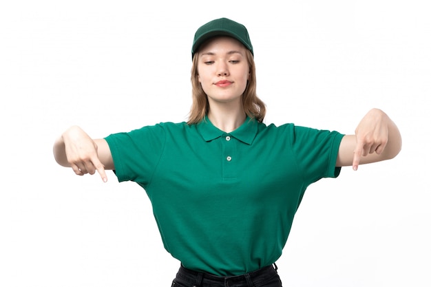 Вид спереди молодая женщина-курьер в зеленой форме позирует с указывая пальцами улыбается