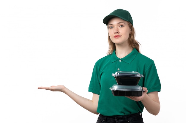 A front view young female courier in green uniform smiling holding black bowls with food